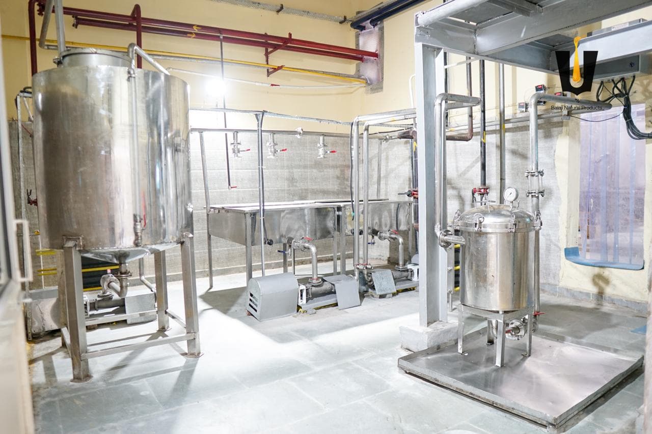 Stainless steel filtration tanks, open settling vats, and pumps in the honey process room