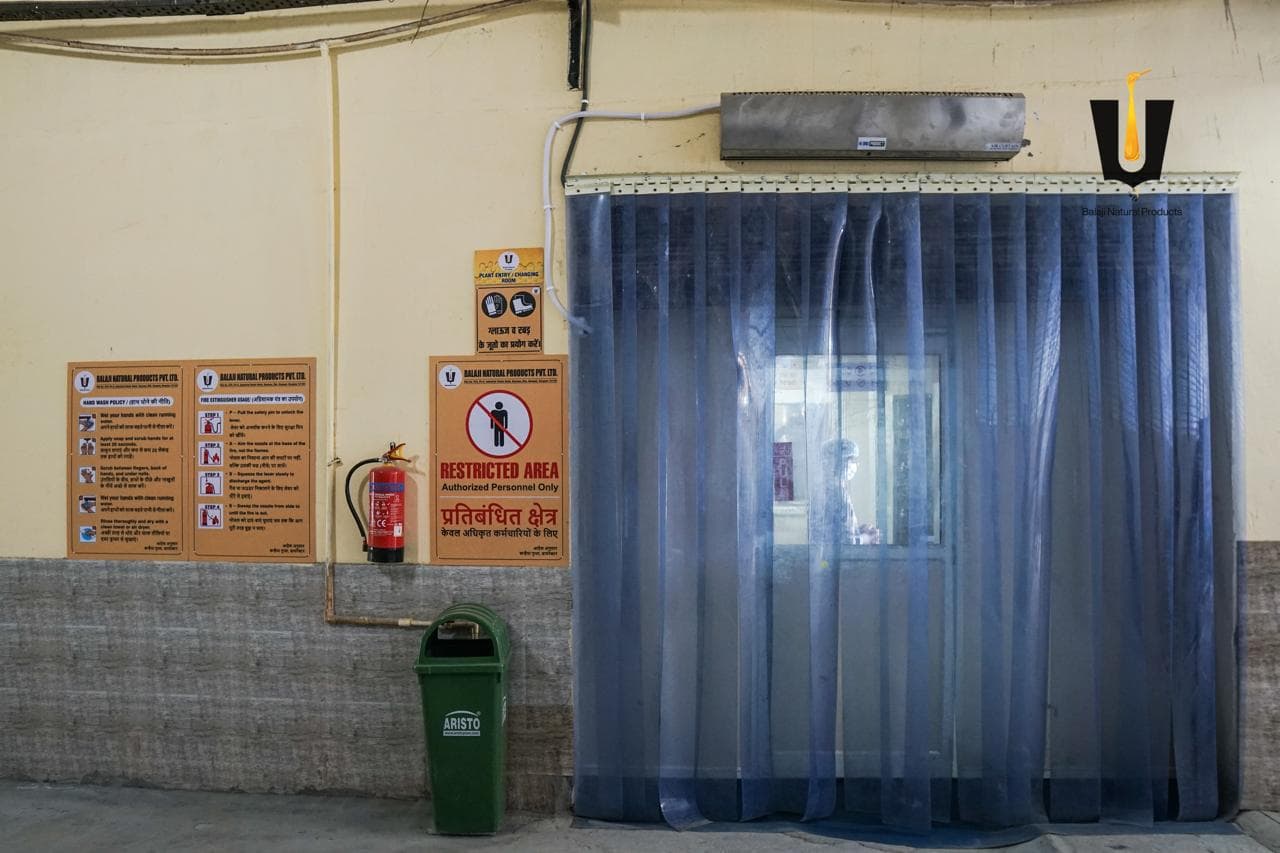 Restricted-area entrance with blue strip curtains, air curtain, and hand-wash policy boards at the honey plant
